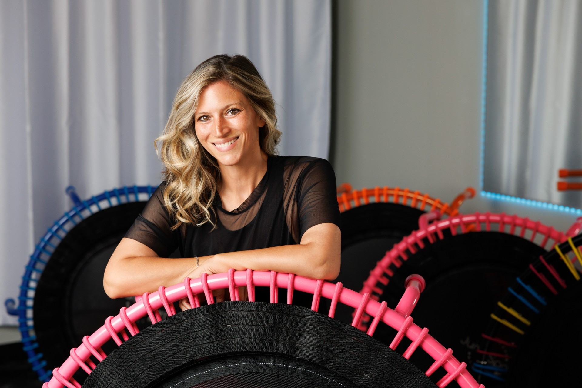 Coach smiling behind a pink rebounder in the studio with colorful rebounders in the background